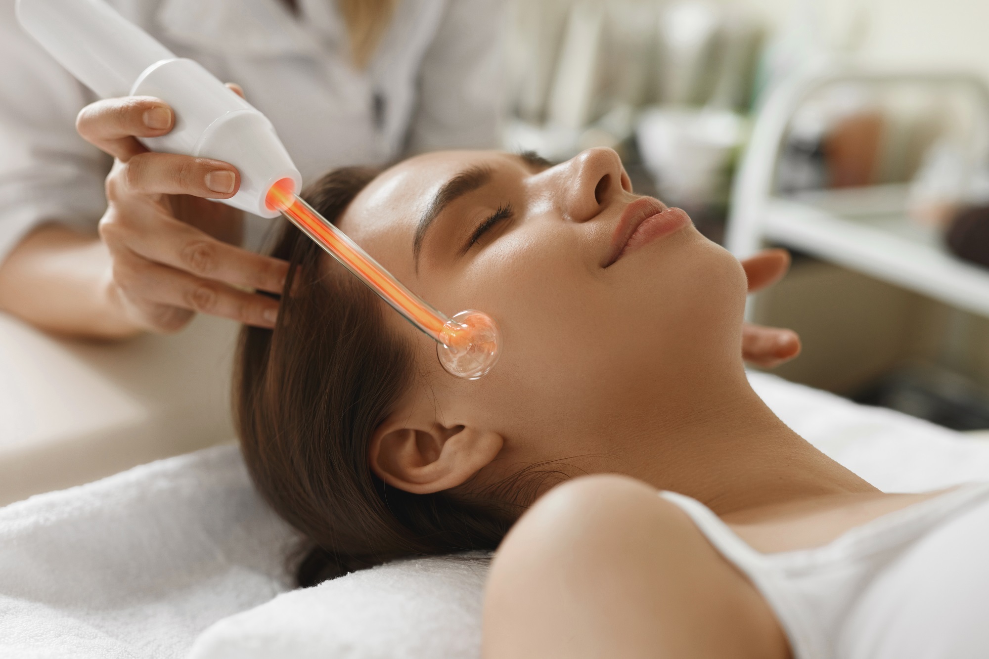 Leticia gliding a high frequency wand across a client's cheek during a facial